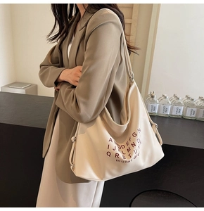 Close-up of a stylish beige tote bag with a brown alphabet pattern and metal buckle detail