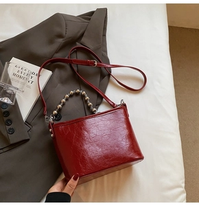 Detail of red bucket bag with metallic bead handle and vintage glossy leather texture
