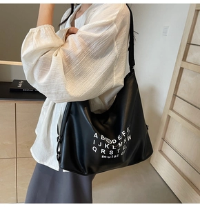 Detail of black leather tote bag showing white lettering and adjustable shoulder strap