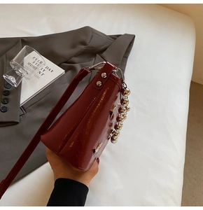 Detail of a dark red patent leather bucket bag with silver bead handle and rivets