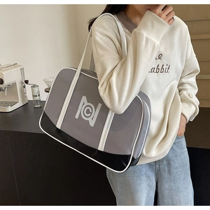 Detail of grey and black patchwork tote bag with white logo carried by a model