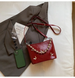 Detail of red glossy leather shoulder bag with silver butterfly buckles and beaded chain