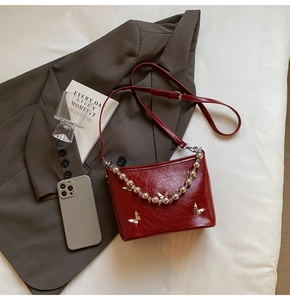 Detail of red pleated leather shoulder bag with silver butterfly and beaded chain charm