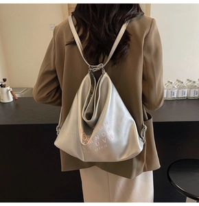 Silver metallic triangular backpack with pink lettering shown on model in a soft lit room