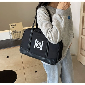 Detail of a large black nylon boston bag with white logo carried by a model