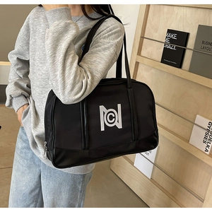 Detail of the black nylon tote bag with white logo worn by a model in a urban style