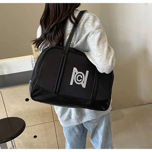 Close-up of a black nylon tote bag with white logo carried by model in a stylish room