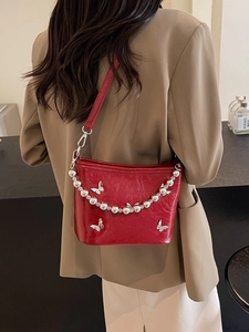 Glossy red shoulder bag with silver butterfly charms worn by model in suit