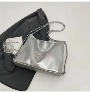 Detail of silver metallic tote bag with pink letter print on a grey blazer background