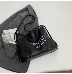 Close-up of black leather tote bag with white alphabet print on a gray blazer