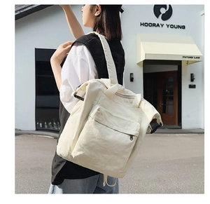Close-up of cream canvas tote backpack with wide handles and a large front zipper pocket