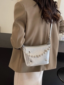 Silver metallic crossbody bucket bag with butterfly charms and beaded chain on a model
