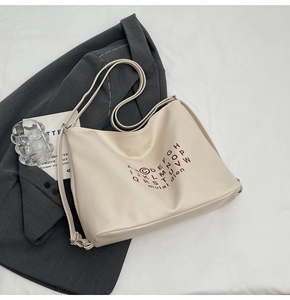 Close-up of cream leather tote bag featuring red circular typography on grey blazer