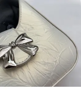 Détail macro d'un sac en similicuir plissé blanc perle avec un nœud en métal argenté