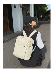 Detail of off-white canvas tote backpack showing top handle and front zipper pocket
