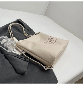 Detail of cream white tote bag with letter print and silver adjustable buckle on a bed