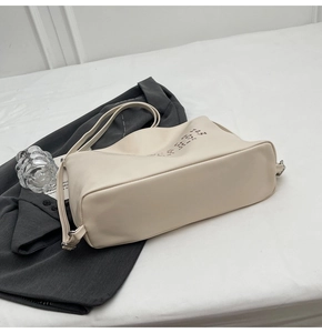 Detail of cream leather tote bag with minimalist lettering on a grey suit background