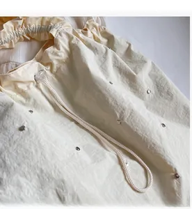 Detailed shot of beige drawstring tote showing pleated fabric and metal rivet accents