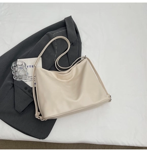 Detail of a beige PU leather hobo bag on a white table with a stylish blazer backdrop