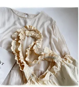 Detail of cream-white fabric handbag with ruffle handles and pleated texture design