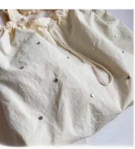 Detail of creamy drawstring tote bag featuring silver rivet accents and soft textured fabric