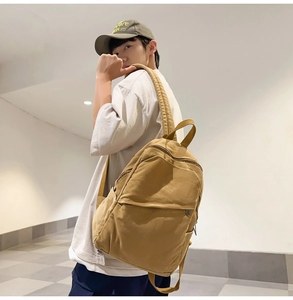 Detail view of mustard yellow canvas backpack worn by model showing side profile and large capacity