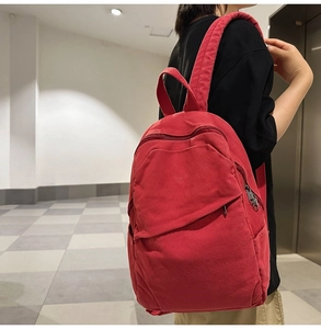 Side view of a large red canvas backpack worn by a model in a modern urban setting
