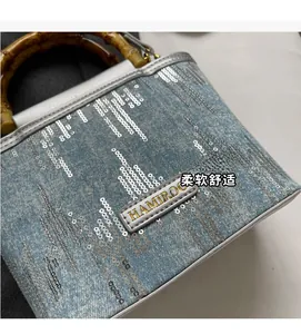 Detail of light blue denim bucket bag with silver sequins and bamboo top handle