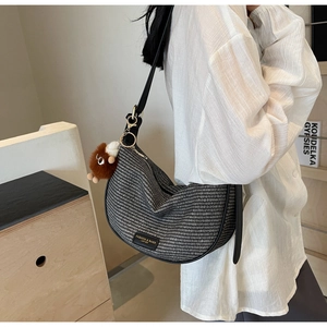 Detail of woven half-moon bag featuring black leather trim and a cute brown plush charm