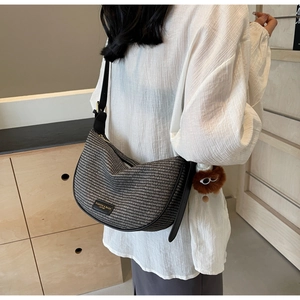 Model wearing a woven half-moon crossbody bag with a plush bear charm detail
