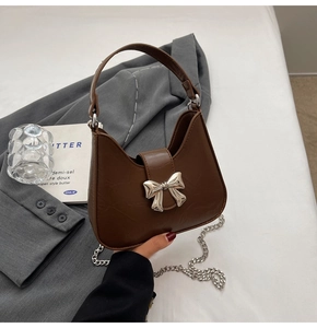 Détail d'un sac porté épaule en similicuir marron avec nœud argenté et bandoulière chaîne