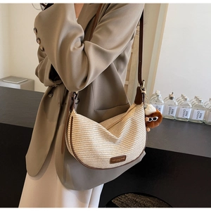 Close-up detail of beige woven dumpling bag with brown leather trim and plush charm