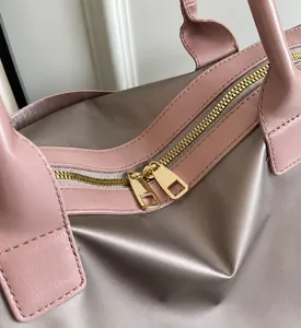 Close-up of smooth gold metal dual zippers on a champagne grey travel bag with pink leather trim