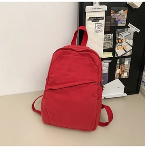 Detail of red canvas backpack featuring diagonal front zipper and side pocket design