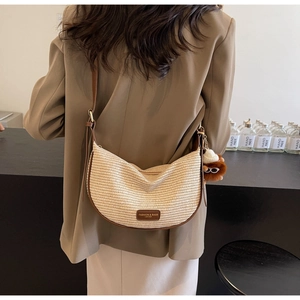 Chic woven half-moon crossbody bag with leather trim and plush pendant worn by a model