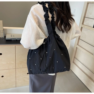 Detail of black nylon tote bag featuring ruffled shoulder strap and silver bead accents