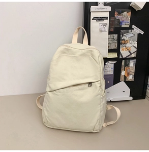 Detail of off-white canvas backpack showing the large front pocket and multi-pocket layout