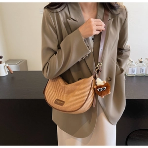 Detail of crescent straw crossbody bag with leather strap and lion plush charm
