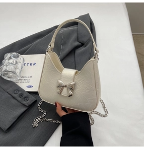 Détail du sac plissé crème avec boucle en nœud argenté et bandoulière en chaîne