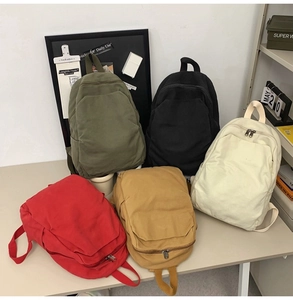 Detailed view of five colorful canvas backpacks in green, black, cream, red, and yellow
