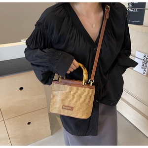 Detail of woven straw bucket bag featuring bamboo handle and leather brand tag