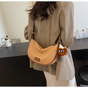 Detail of hand-woven straw hobo bag with leather strap and plush charm on brown blazer