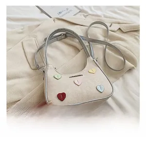 Close-up of beige crossbody bag with colorful heart-shaped studs and silver leather trim