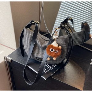 Detail of woven hobo bag with leather strap and cute plush doll accessory on a dark desk