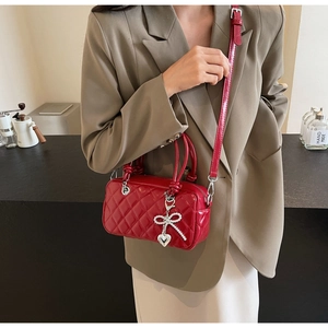Detail of red quilted crossbody bag with diamond bow and heart charm on a female model