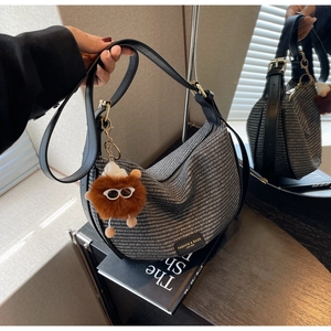 Detail of woven crescent bag with black leather strap and brown plush monster charm