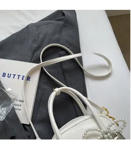 Détail d'un sac coquillage blanc avec texture litchi et nœud de perles décoratif