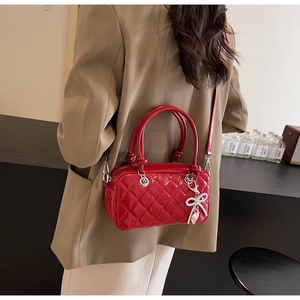 Detail view of red quilted crossbody bag with rhinestone bow charm on a female model