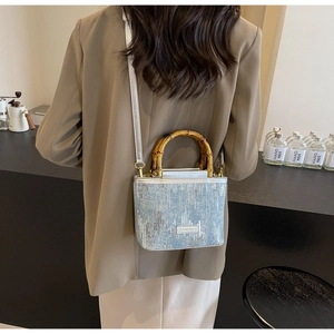 Detail of light blue bucket bag with natural bamboo handle and silver shoulder strap