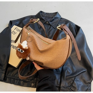 Detail of woven crescent bag with brown leather trim and cute plush doll charm